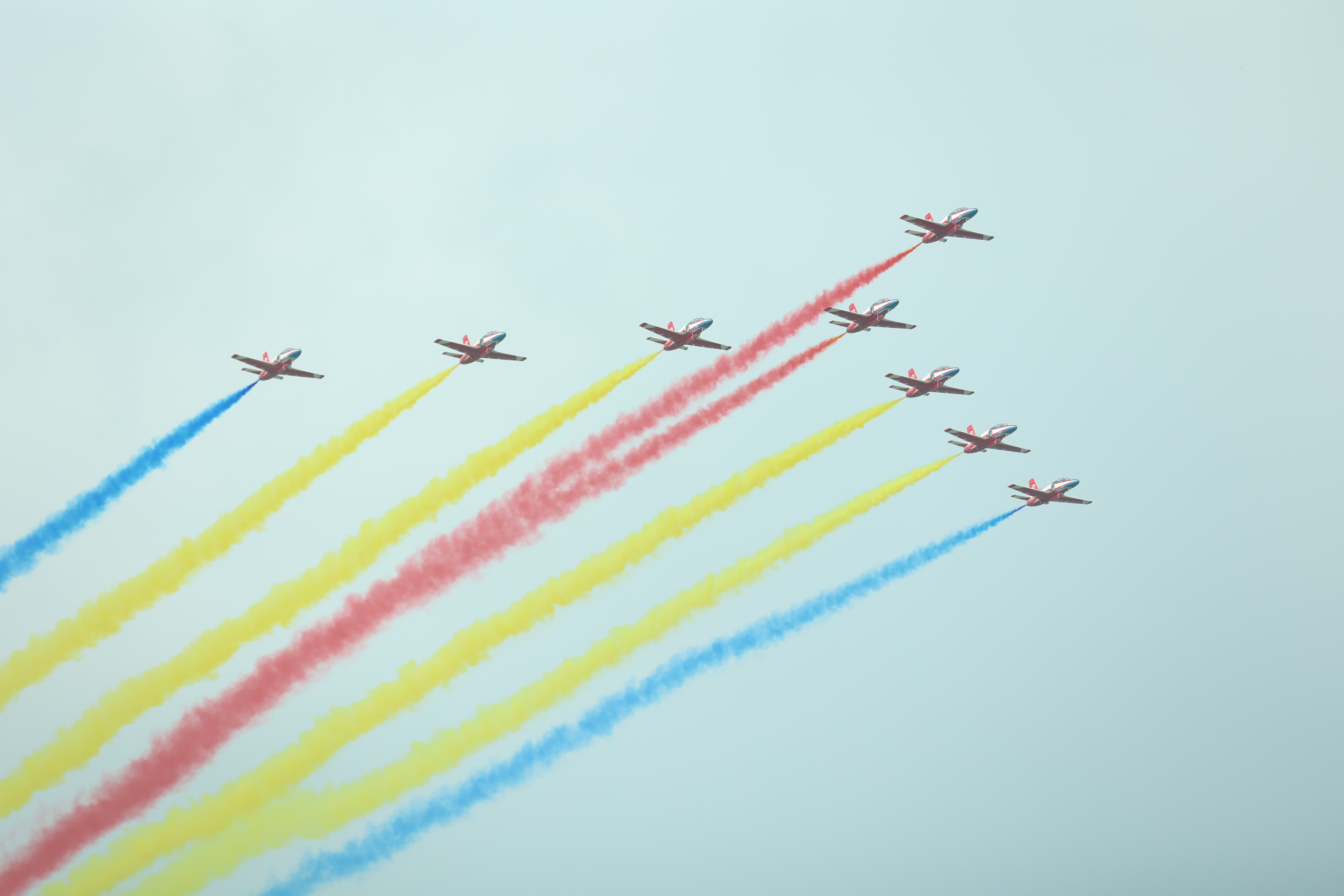 8架飛機以紅鷹隊形通場，拖着彩色的煙帶，宛如一隻雄鷹在藍天起舞。（盧冶攝）