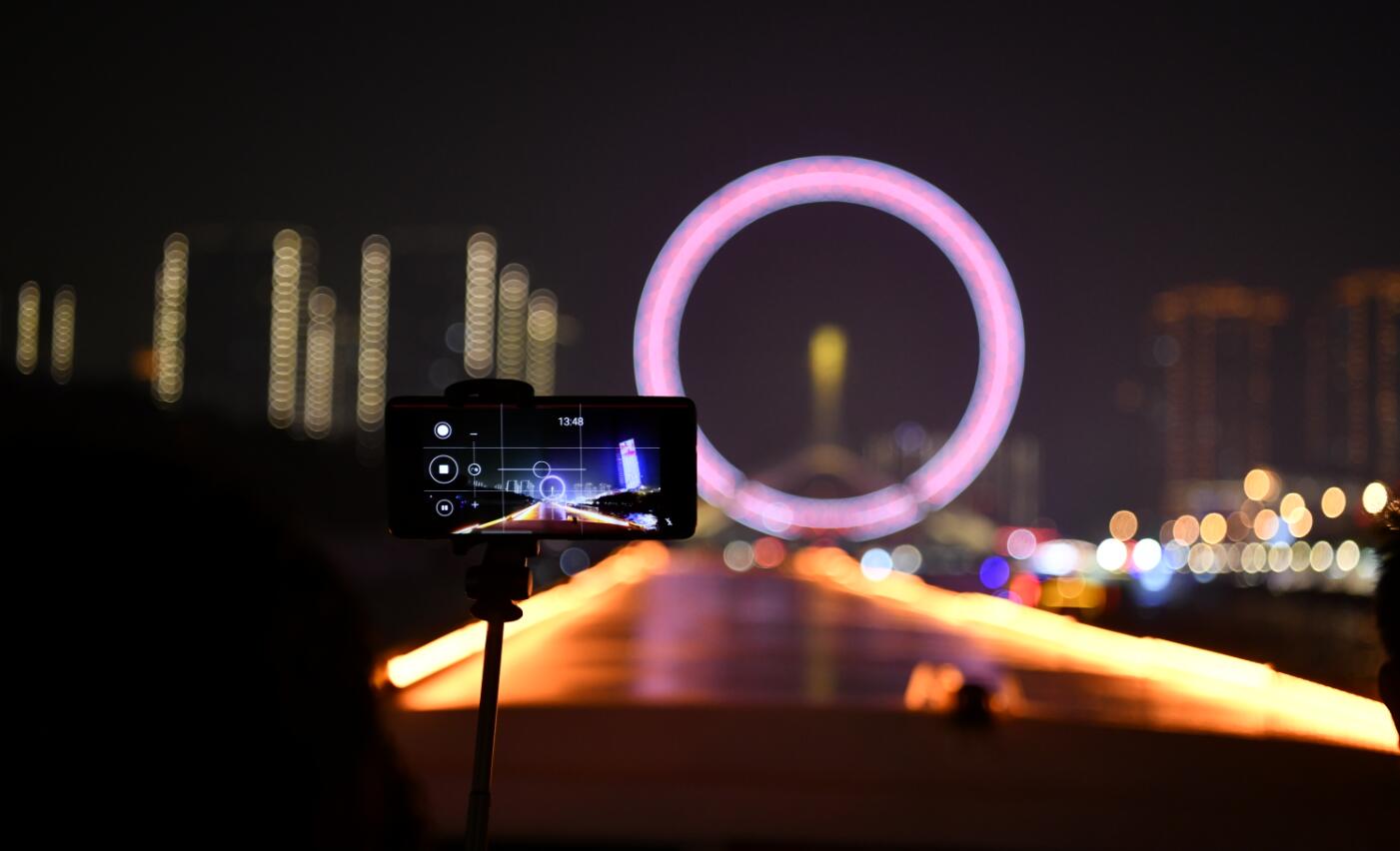 一名遊客在海河遊船上用手機拍攝「天津之眼」摩天輪上的夜景燈光（10月1日攝）。（新華社）