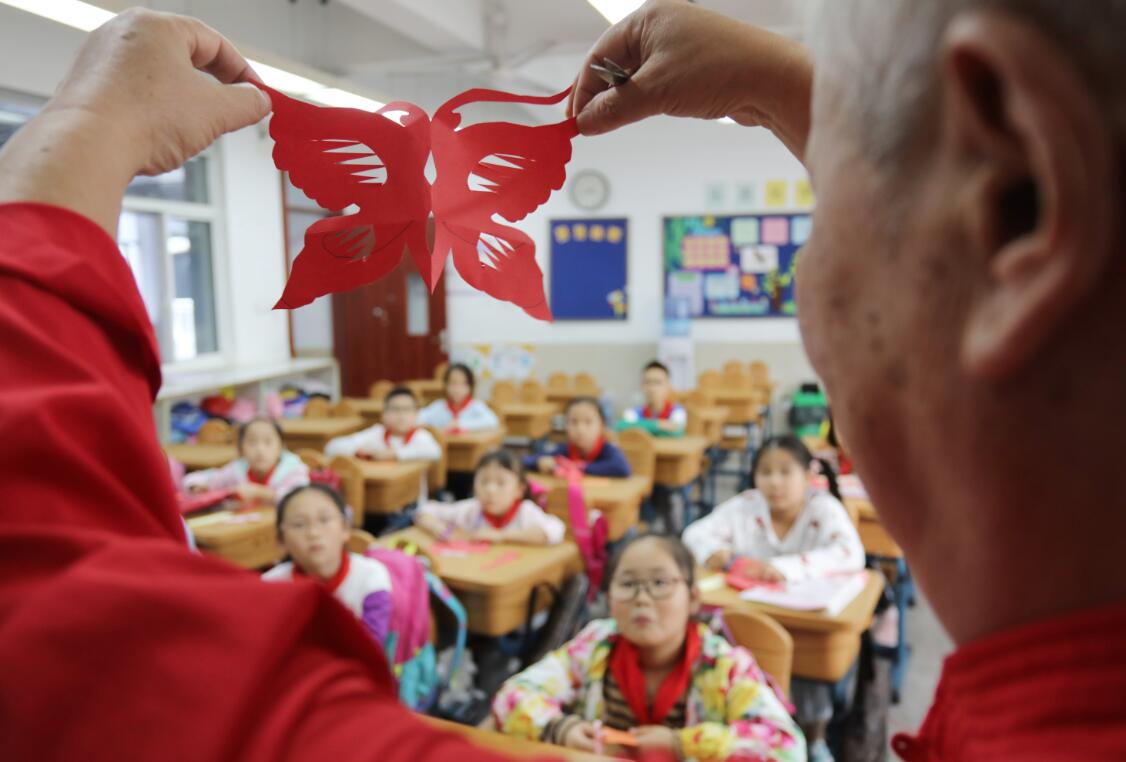 10月9日，民間藝人在蘇州工業園區星海小學向孩子們講解剪紙技藝。（新華社）