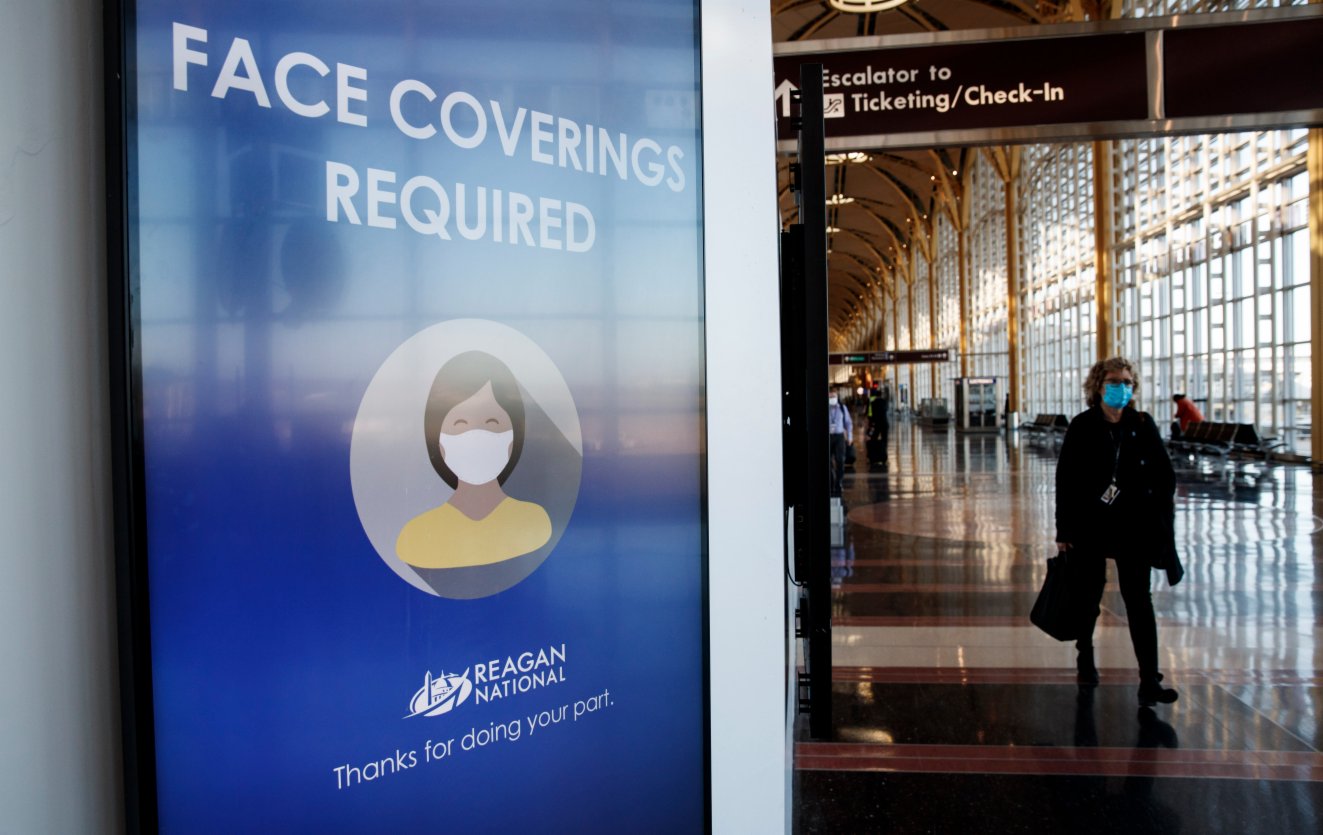 11月24日，在美國弗吉尼亞州阿靈頓的里根國家機場，一名戴口罩的女子走過要求佩戴口罩的標識。（新華社）