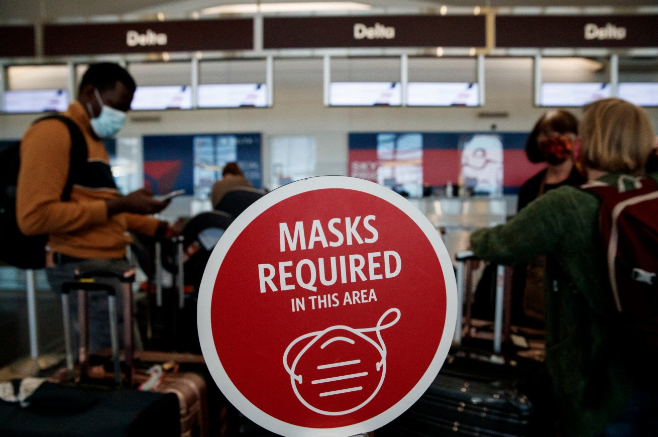 11月24日，在美國弗吉尼亞州阿靈頓的里根國家機場，戴口罩的旅客們站在一處要求佩戴口罩的標識旁。（新華社）