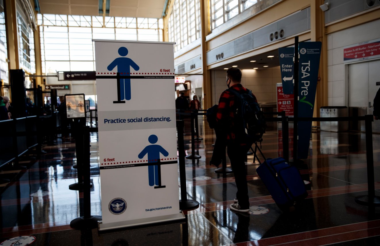 11月24日，在美國弗吉尼亞州阿靈頓的里根國家機場，戴口罩的旅客們站在一處要求佩戴口罩的標識旁。（新華社）