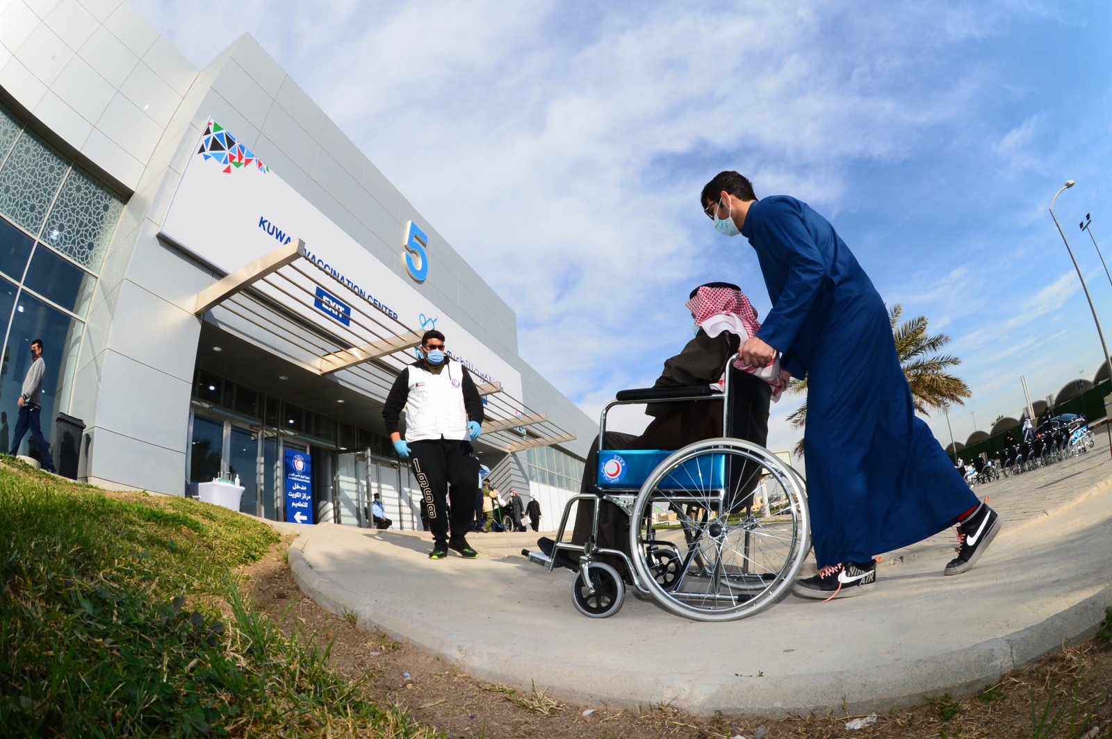 1月14日，在科威特哈瓦利省的新冠疫苗接種中心，一名老人坐輪椅前往接種第二劑新冠疫苗。（新華社）