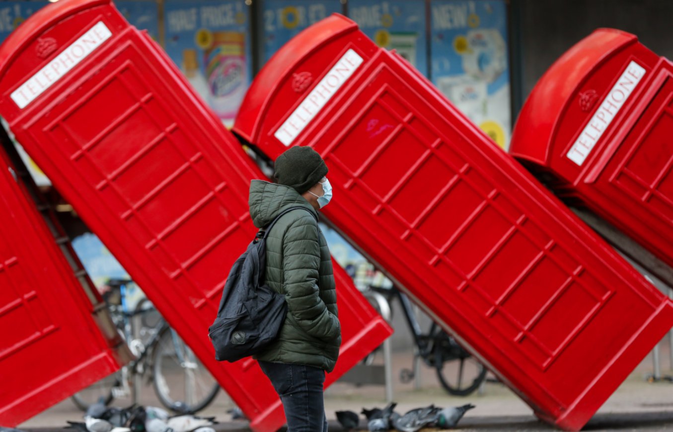 1月21日，一名戴口罩的男子從英國泰晤士河畔金斯頓街頭的紅色電話亭雕塑旁走過。（新華社）