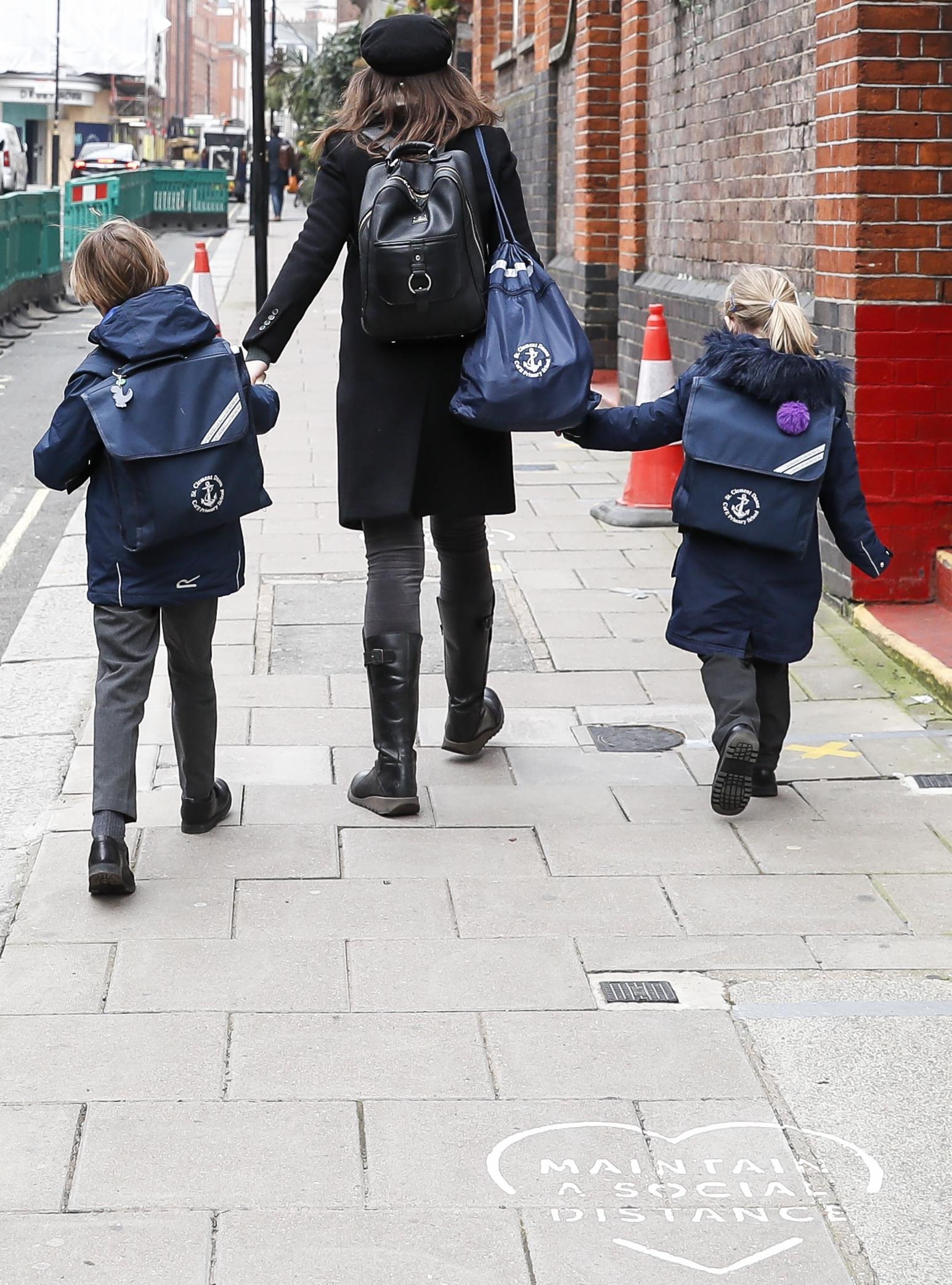 3月8日，英國倫敦一名女子送孩子上學時走過街道上提示保持社交距離的標識。