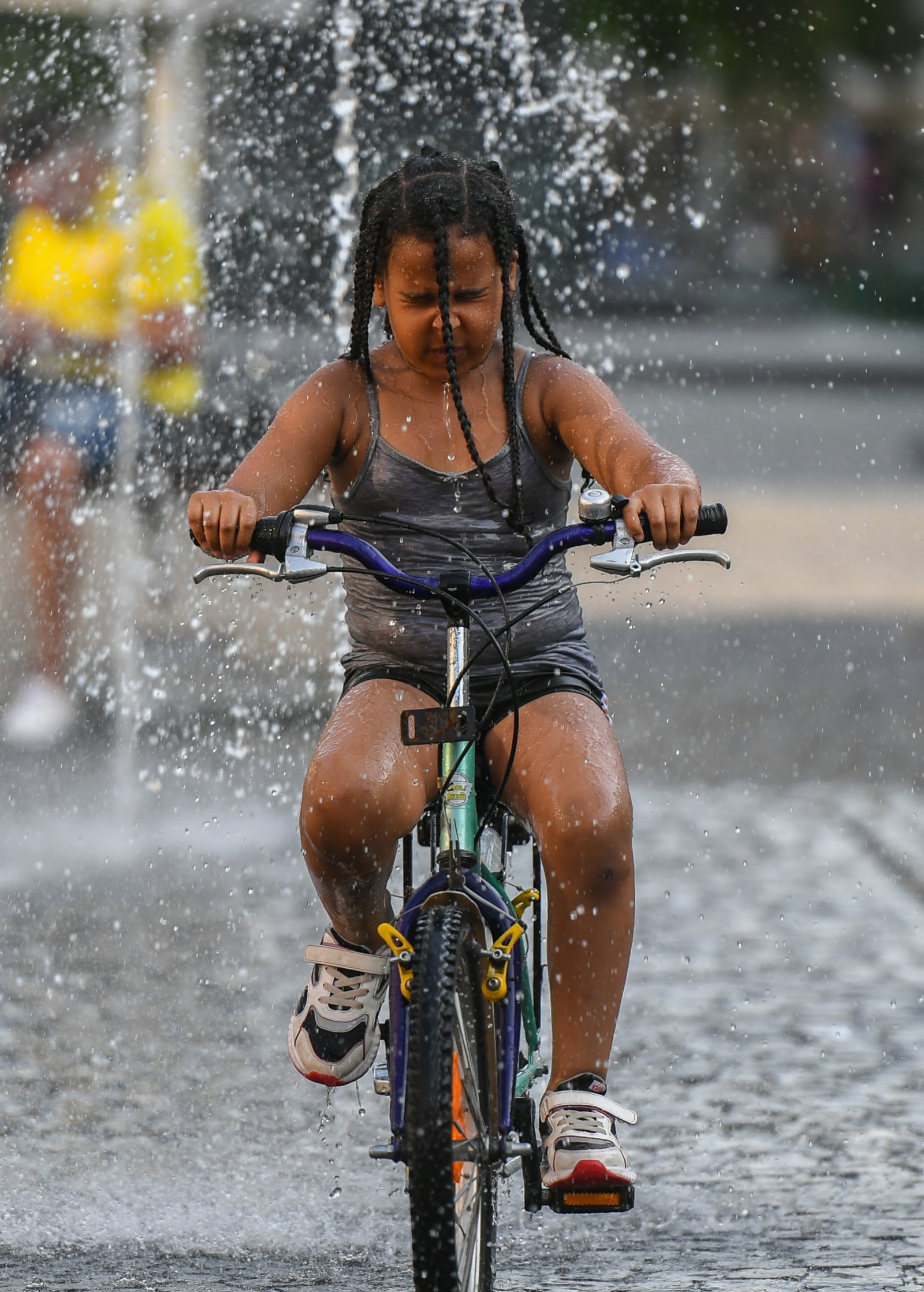 6月17日，在德國法蘭克福，一名小朋友騎車穿過噴泉納涼。（新華社）