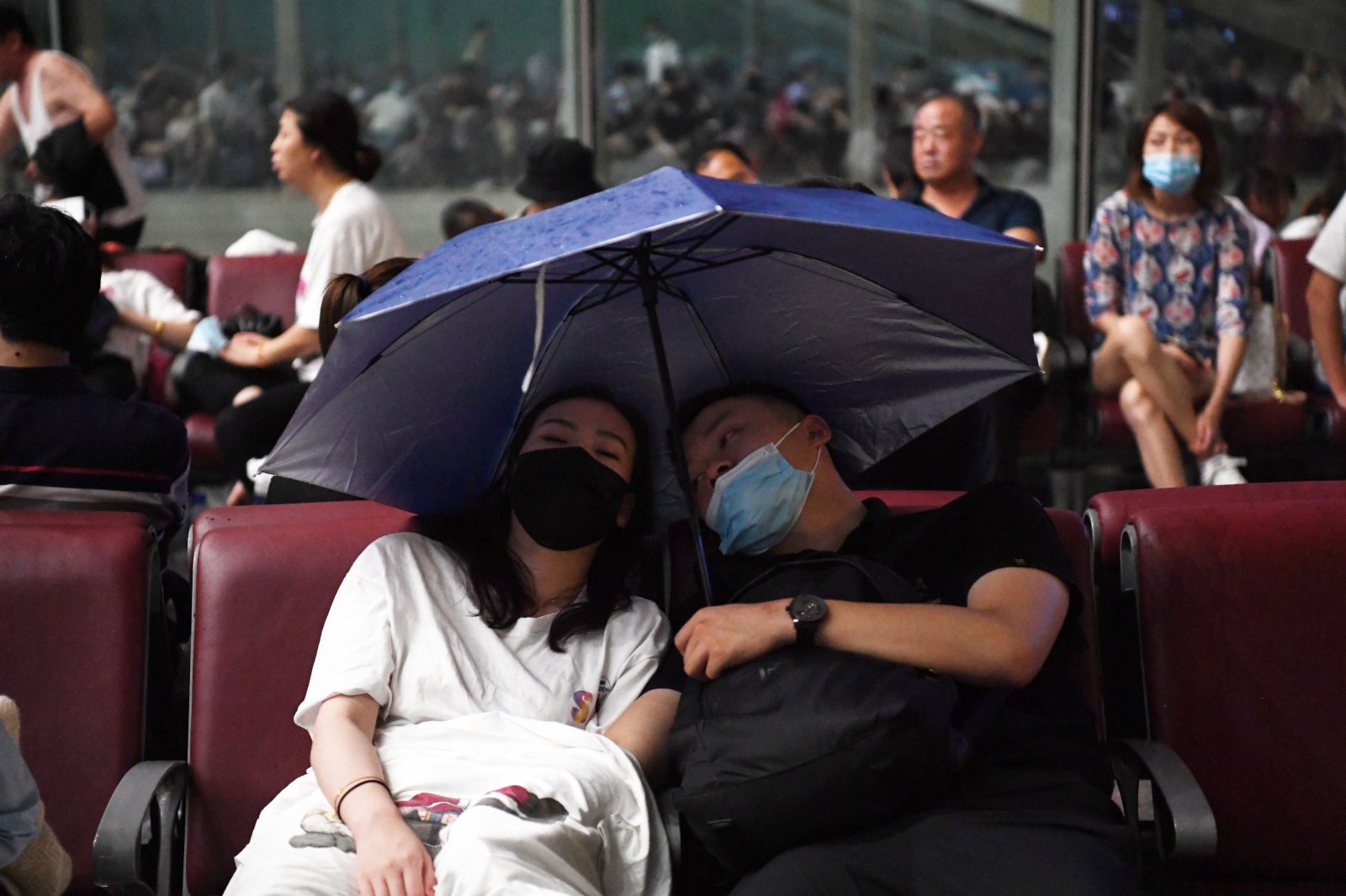 7月20日，旅客滯留在鄭州東站。候車廳出現漏雨情況，旅客撐傘擋雨。（新華社）