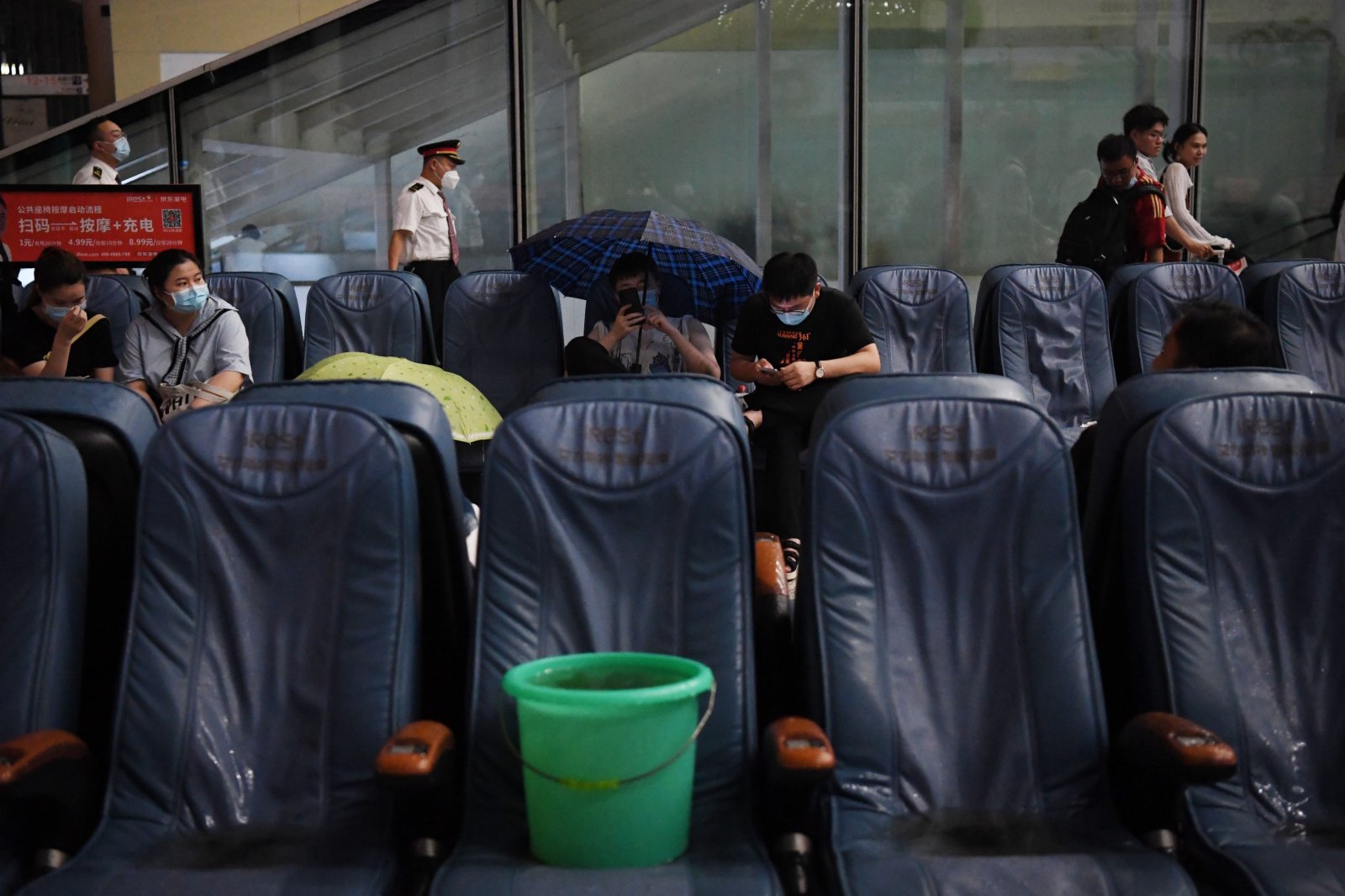 7月20日，旅客滯留在鄭州東站。候車廳出現漏雨情況，旅客撐傘擋雨。（新華社）