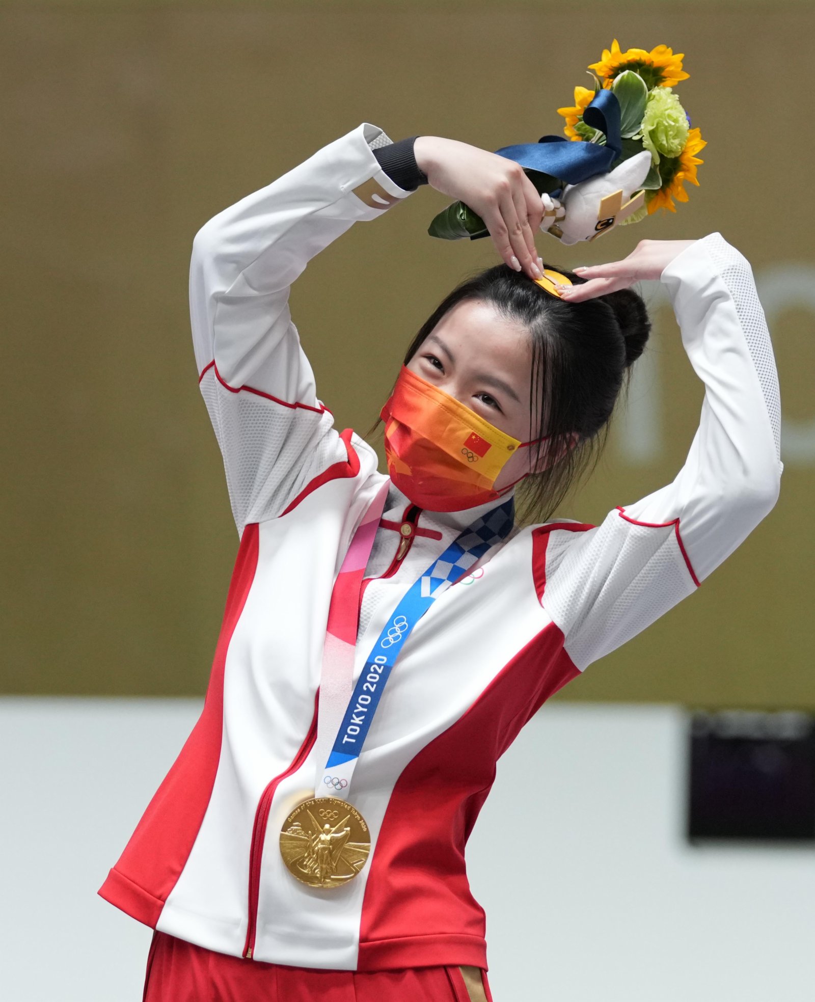 7月24日，在東京奧運會射擊女子10米氣步槍決賽中，中國選手楊倩奪冠，贏得東京奧運會首枚金牌。她在領獎台上「比心」。（新華社）