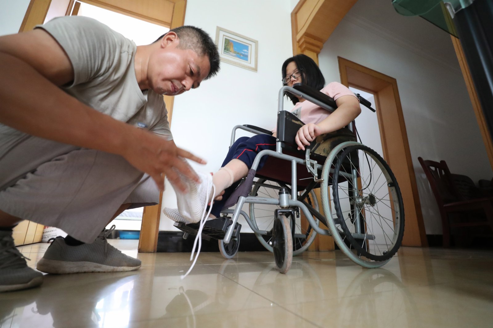 9月1日,謝培軍在家中幫女兒穿好鞋子,準備趕往學校報到。(新華社) 9月1日,謝培軍在家中幫女兒穿好鞋子,準備趕往學校報到。(新華社)