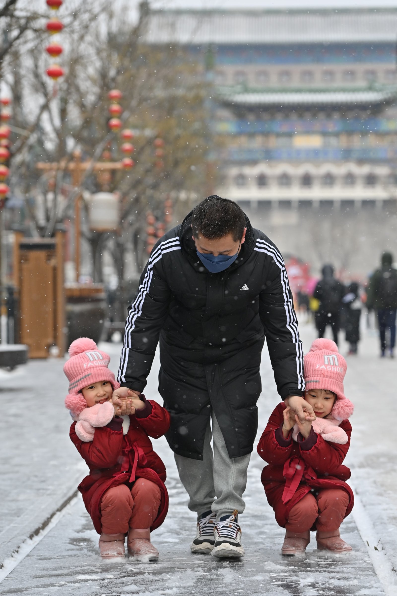 1月20日，在北京前門大街，一對雙胞胎在父親的陪伴下在雪中玩耍。（新華社）