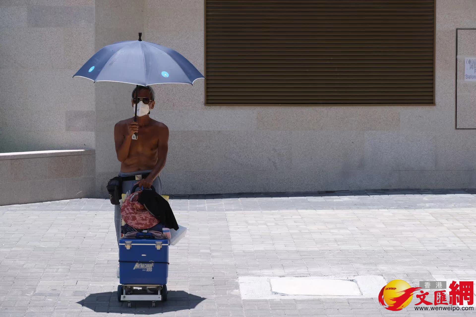 一位市民在烈日下打傘遮陽，防止中暑。