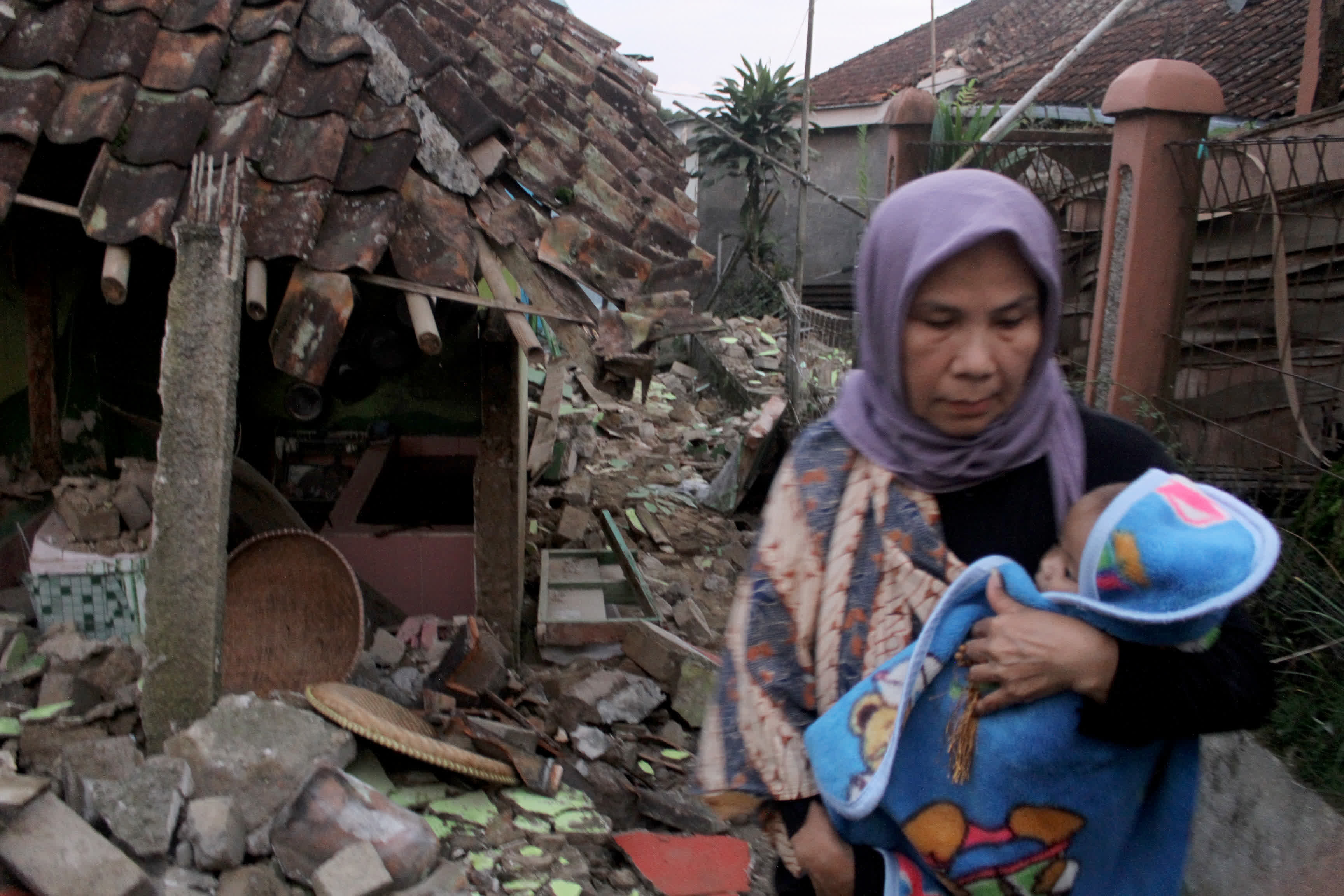 11月21日，在印度尼西亞西爪哇省展玉，一名女子抱着孩子站在被地震損毀的房屋旁。（新華社）