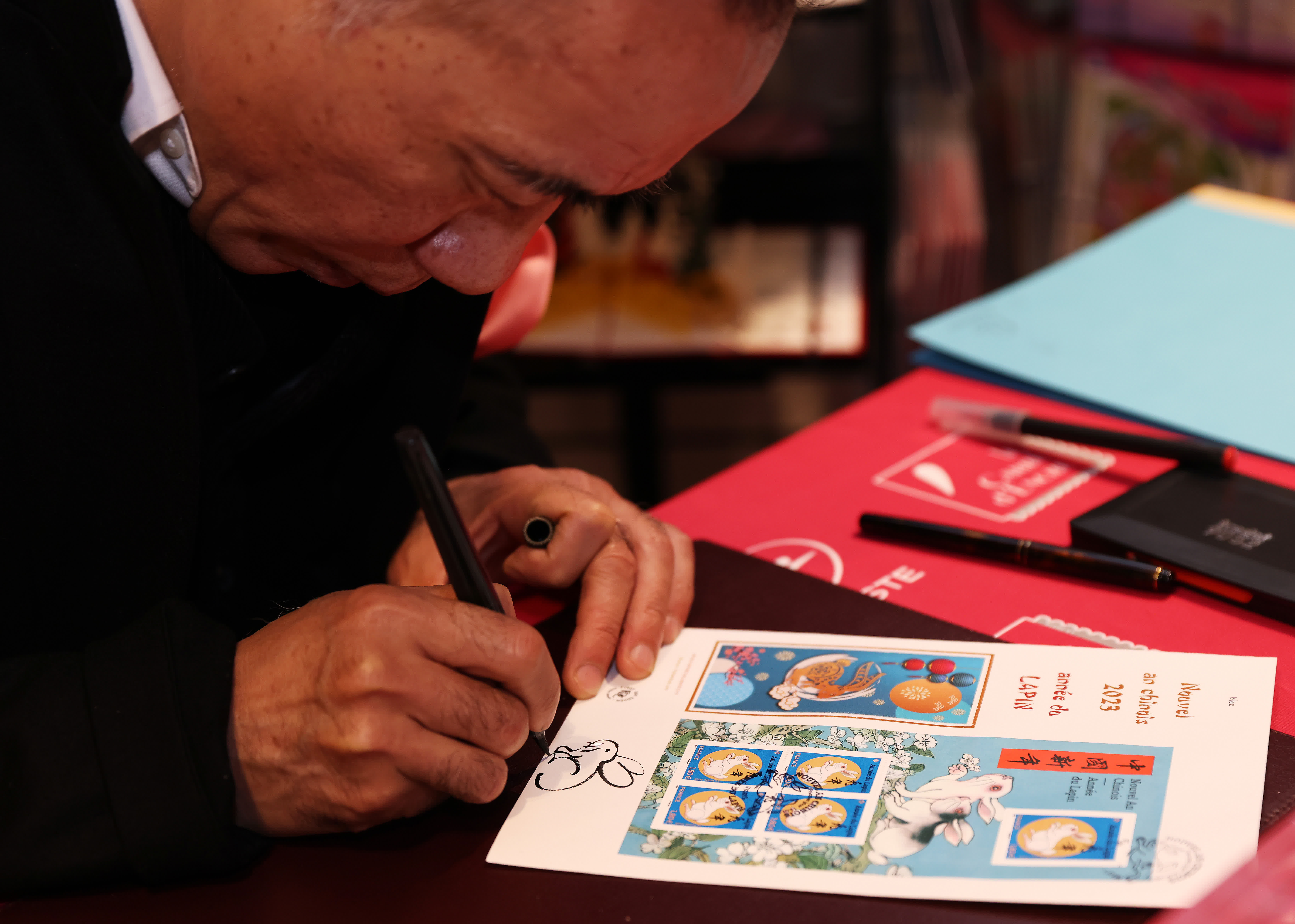 1月14日，在法國巴黎舉行的兔年生肖郵票發行儀式上，郵票設計者陳江洪為集郵愛好者簽售兔年生肖紀念郵票。（新華社）