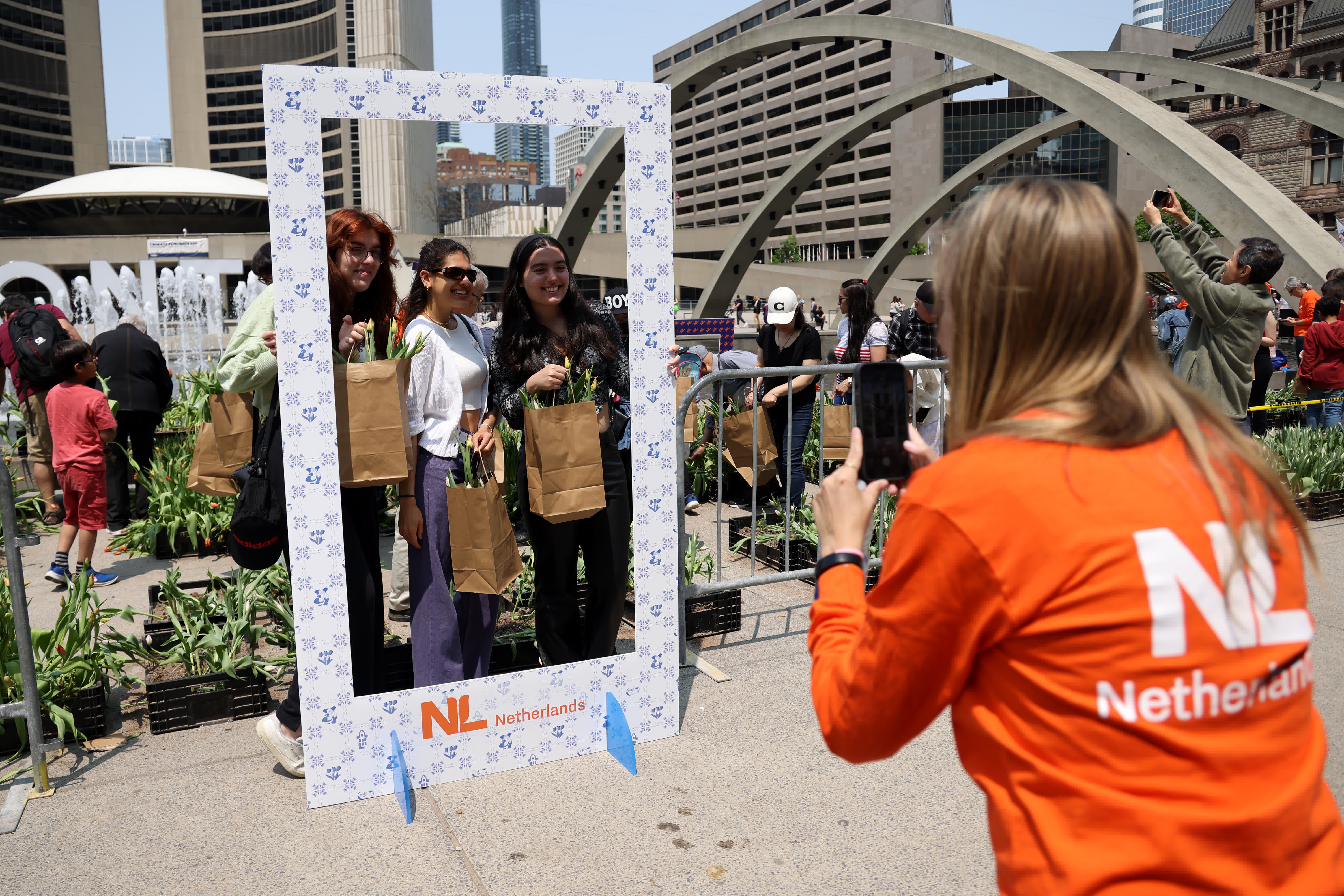 當地時間5月21日，加拿大多倫多，三名年輕女士在市政廳廣場挑選採摘鬱金香花株後合影留念。（中新社）