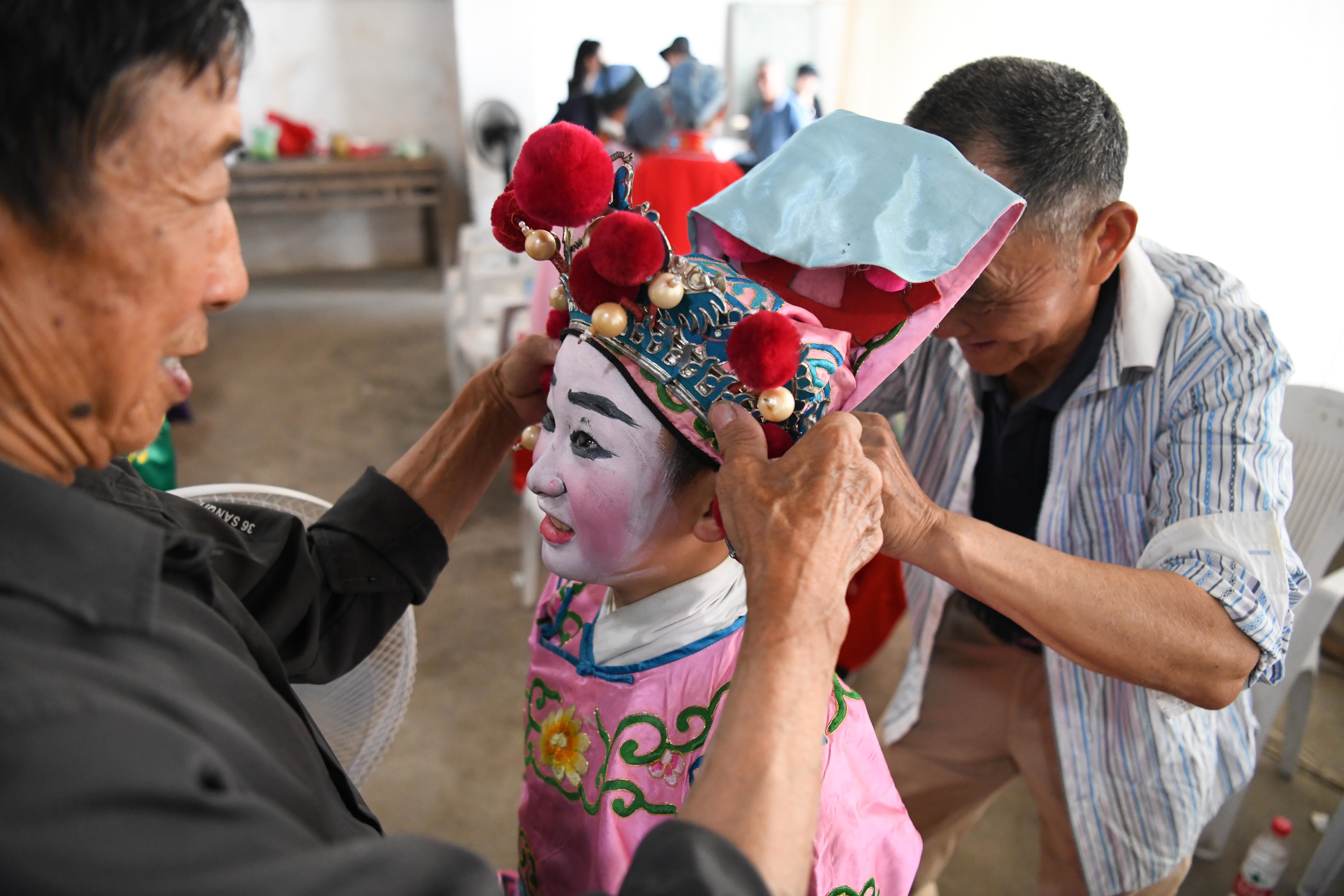 5月30日，民間老藝人在給9歲的伏嶺鎮中心小學「徽劇童子班」學生方冬冬（中）固定頭飾。（新華社）