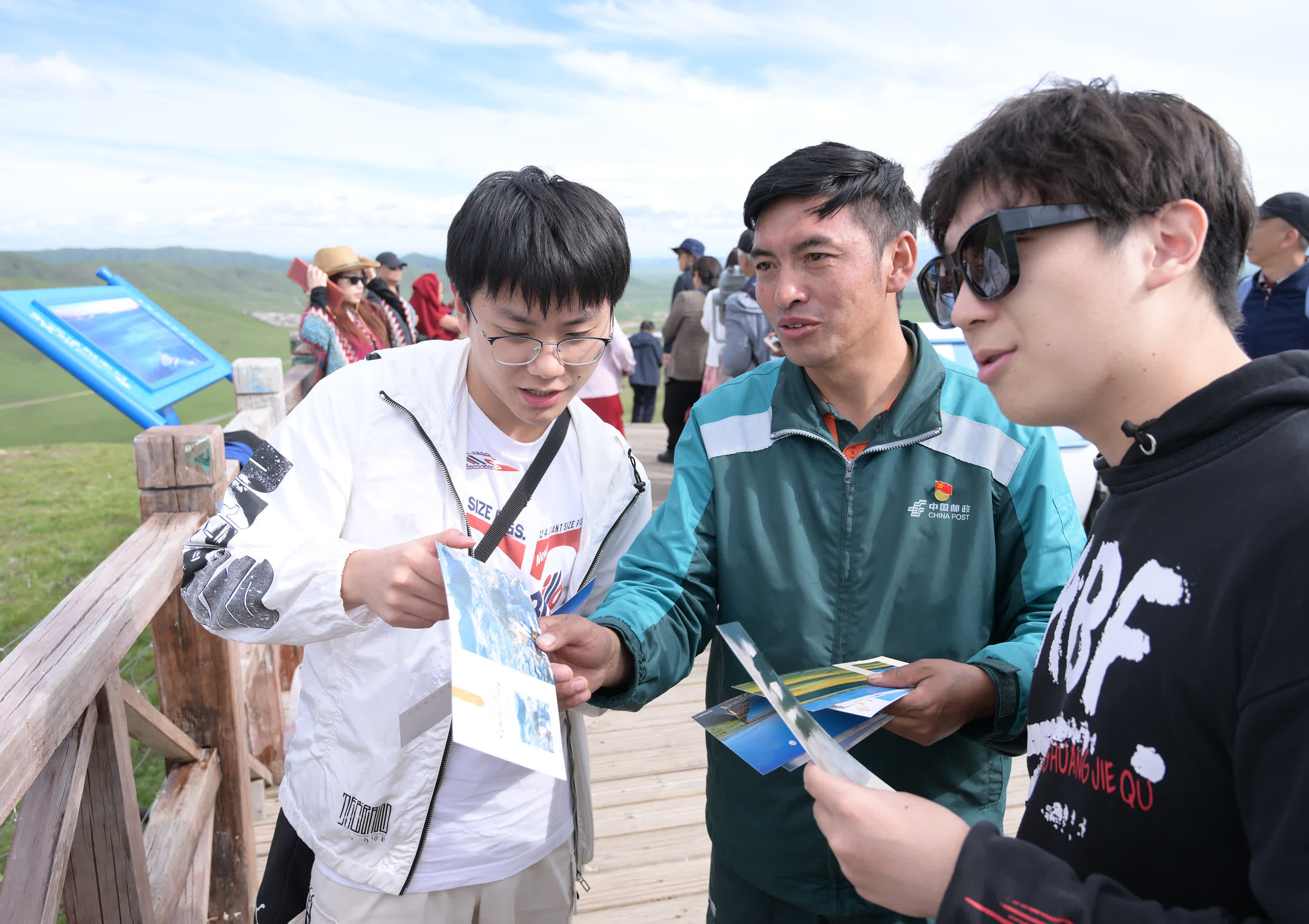 哈弄奪機（中）在若爾蓋縣黃河九曲第一灣景區向遊客發放郵政明信片，宣傳介紹當地旅遊資源。（新華社）