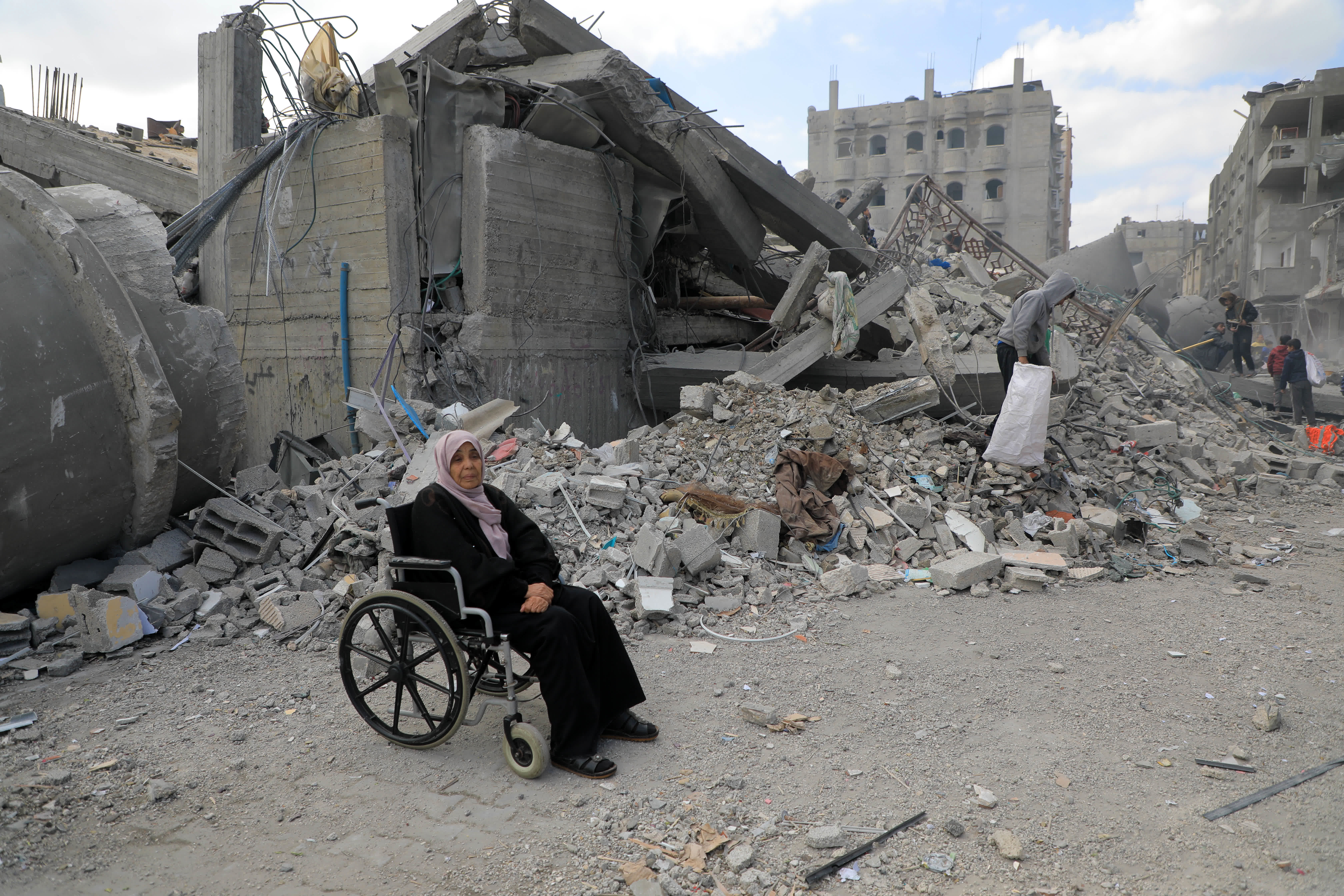 這是2月22日在加沙地帶南部城市拉法一處以軍襲擊後的建築廢墟旁拍攝的一名坐在輪椅上的婦女。（新華社）