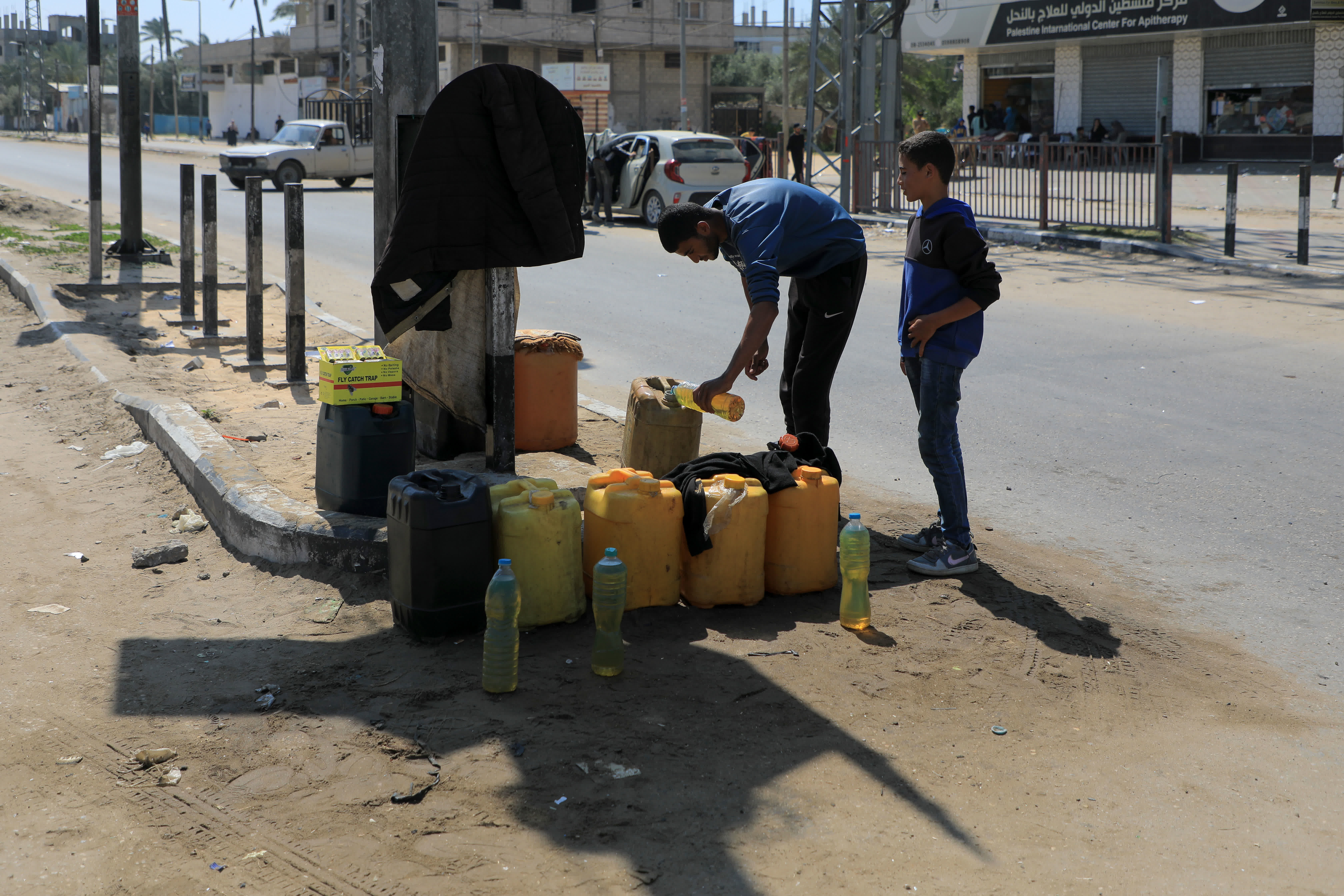 4月16日，在加沙地帶中部城市代爾拜拉赫，巴勒斯坦人正在向油桶裏填充燃料。（新華社）