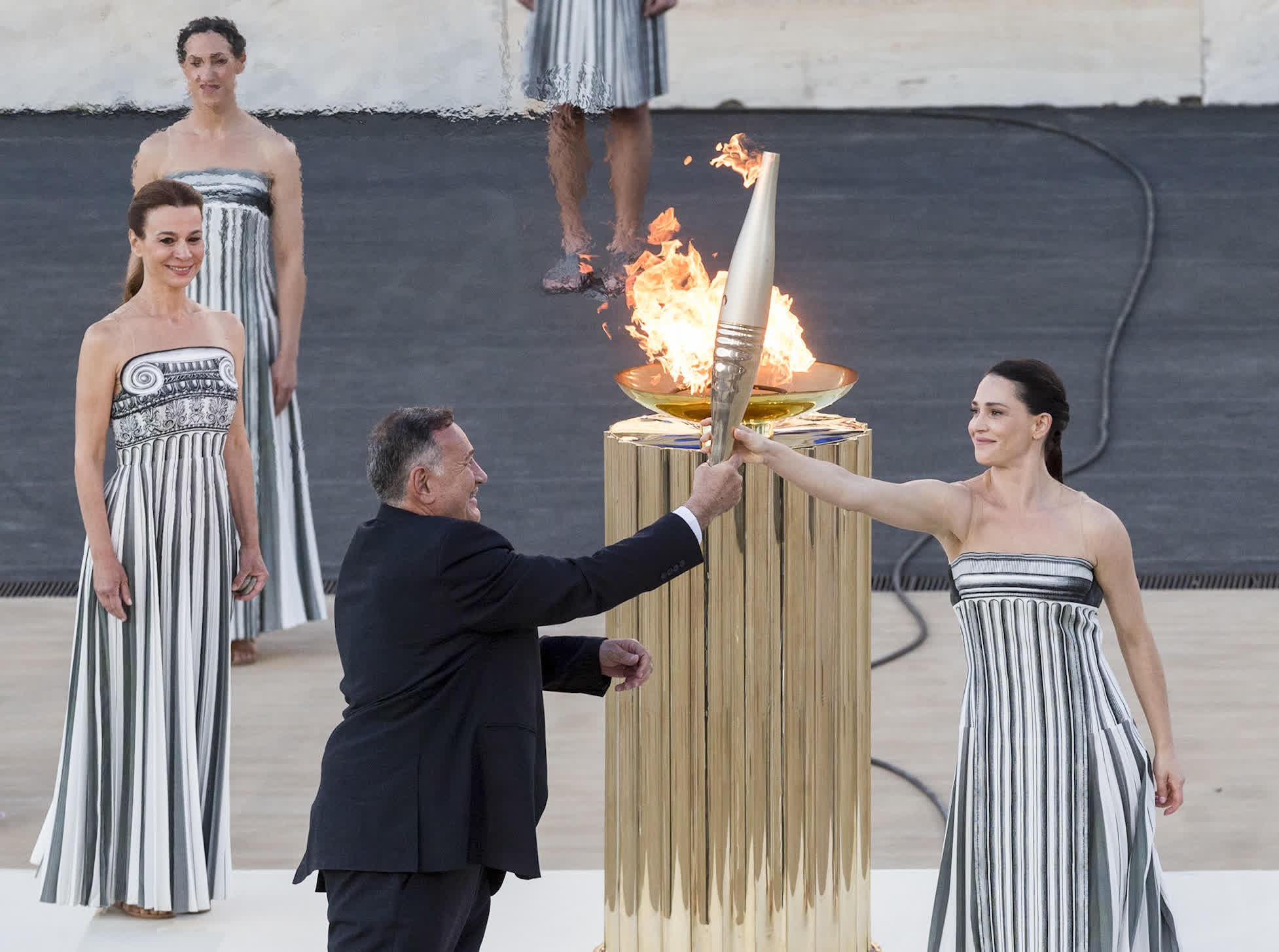 4月26日，希臘奧委會主席卡普拉洛斯（前左）從扮演最高女祭司的希臘女演員瑪麗·米娜手中接過火炬。（新華社）