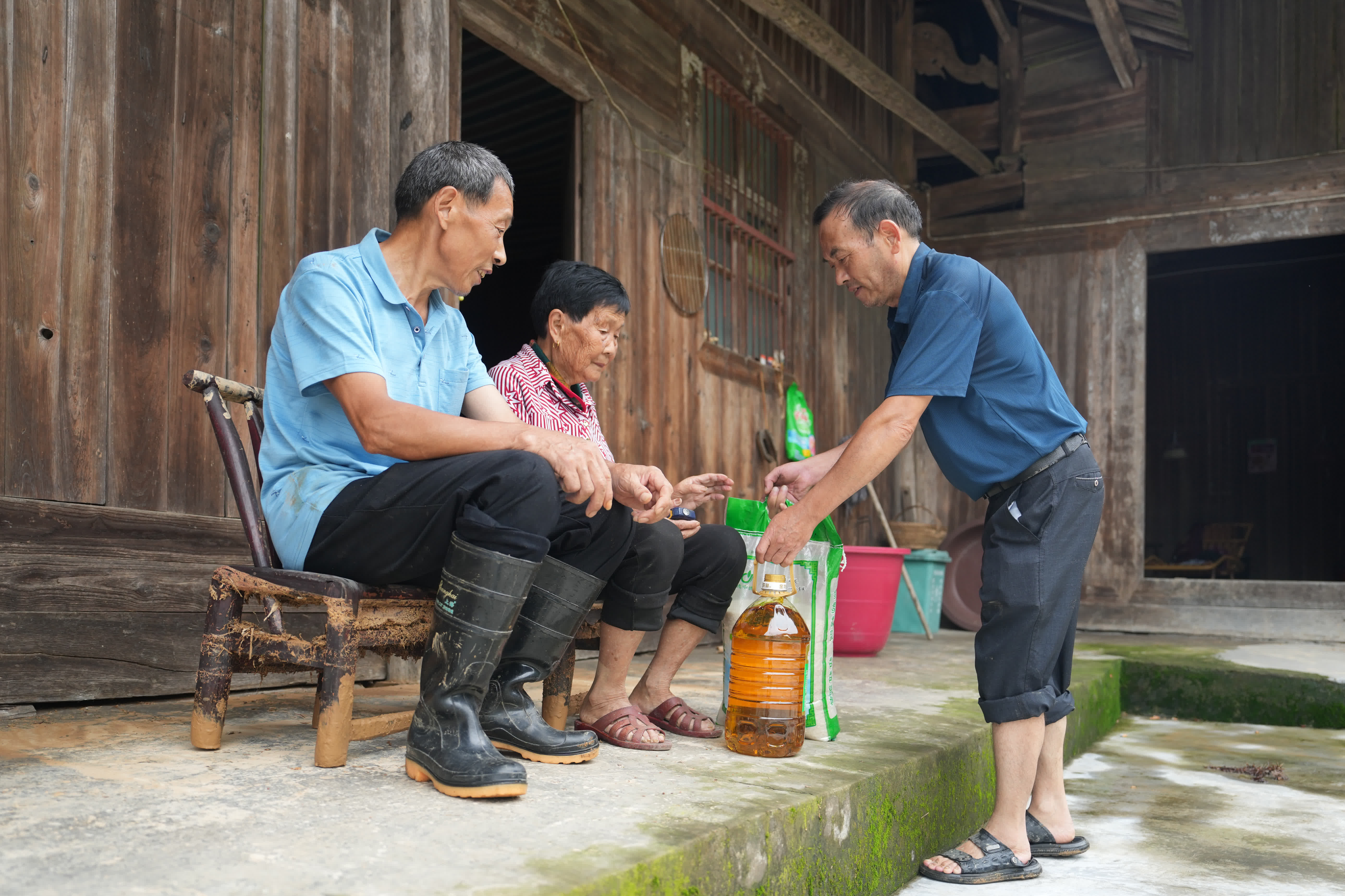 6月25日，志願者（右）將米、油送至一戶(hù)受災村民家中。（新華社）