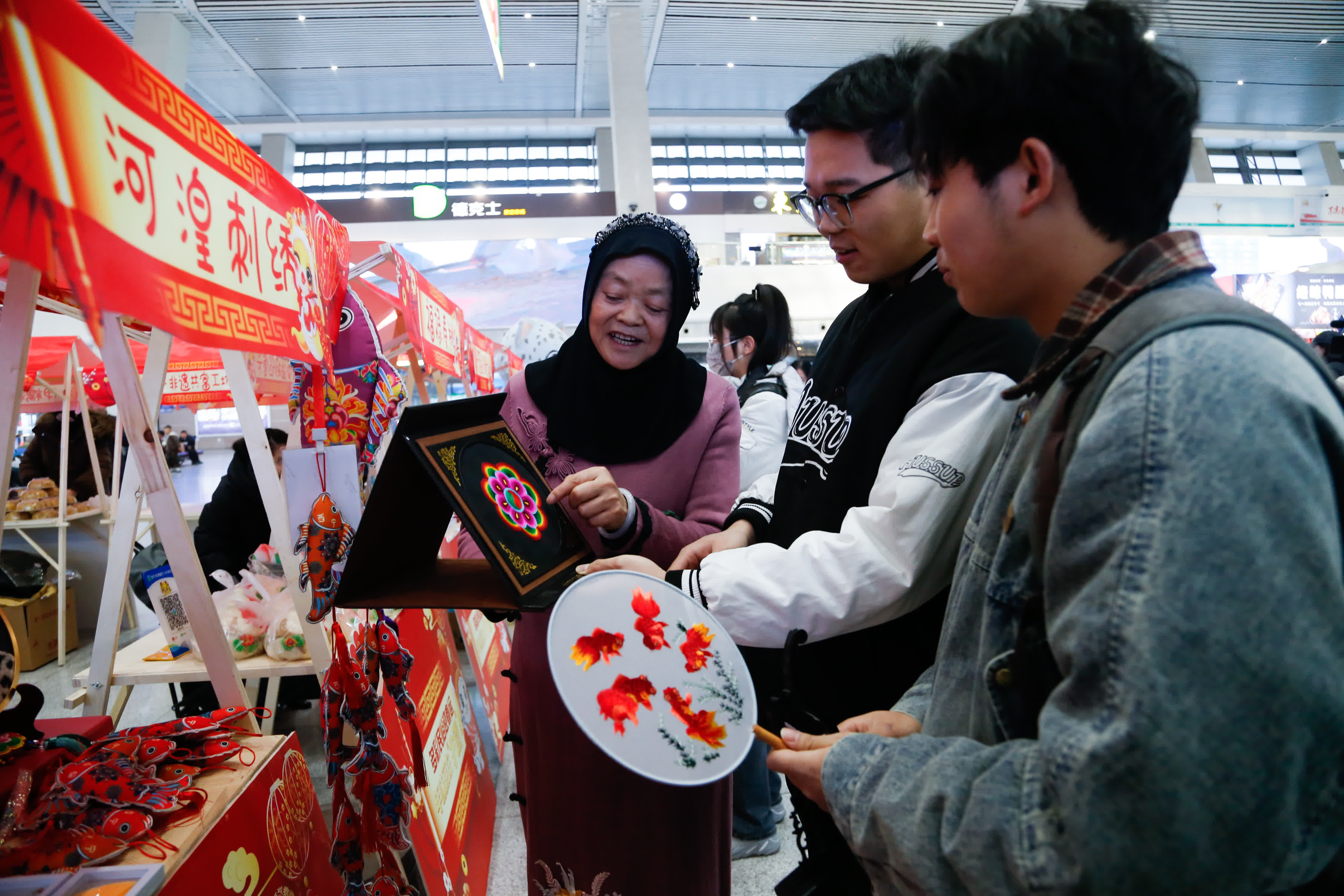 1月14日，西寧火車站，旅客在非遺集市上了解青海。當(dāng)日，2025年春運(yùn)啟幕，青海特色非遺走進(jìn)火車站，裝扮列車車廂，吸引過往旅客關(guān)注了解。 中新社