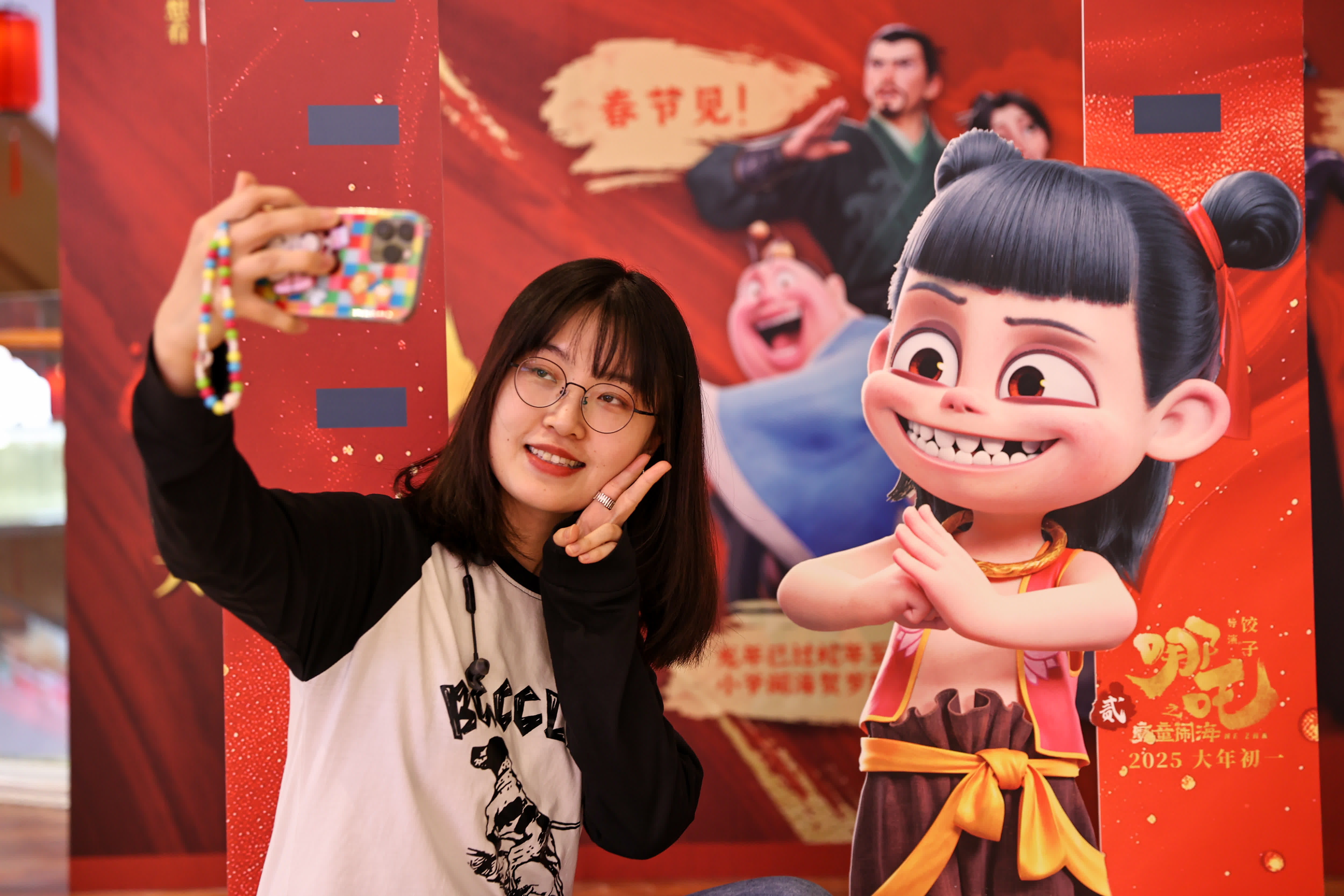 2月12日，遼寧瀋陽玖伍文化城推出一系列與《哪吒之魔童鬧海》相關的文化活動。圖為市民在《哪吒之魔童鬧海》電影海報展板前合影。（中新社）