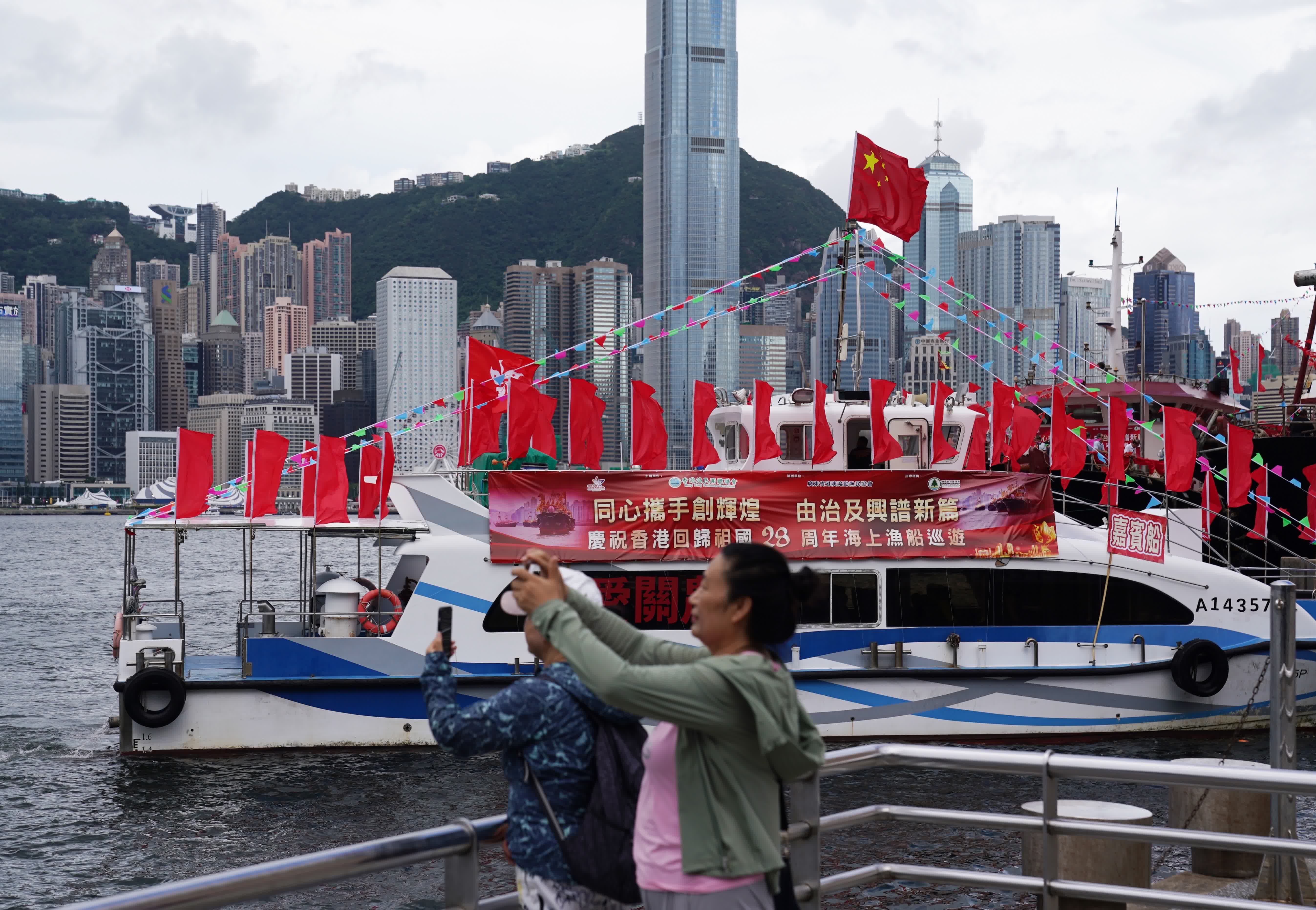 7月1日，市民在香港尖沙咀海濱拍攝巡遊的漁船。（新華社）