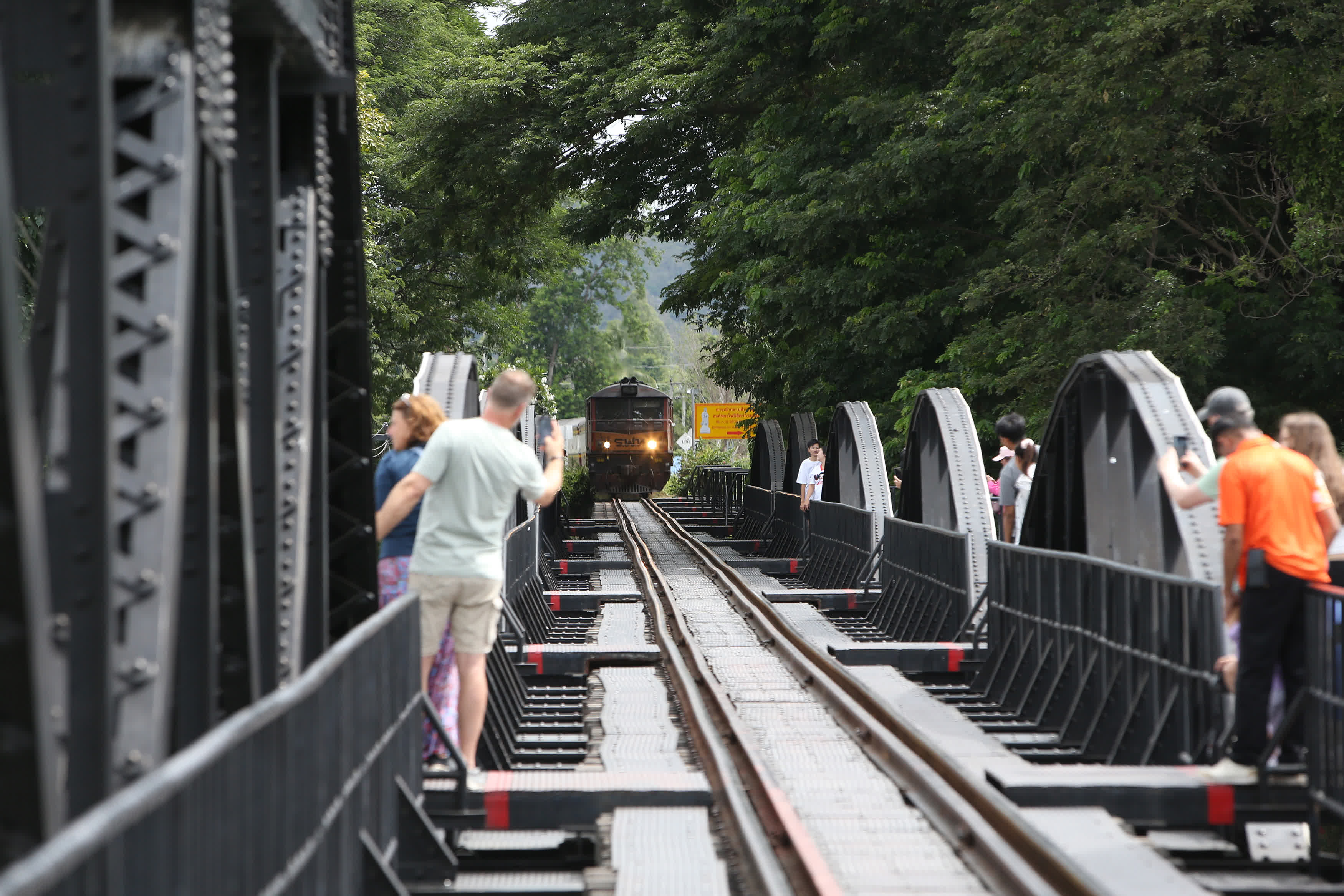 8月13日，遊客在泰國北碧府桂河大橋上拍攝駛近的火車。（新華社）
